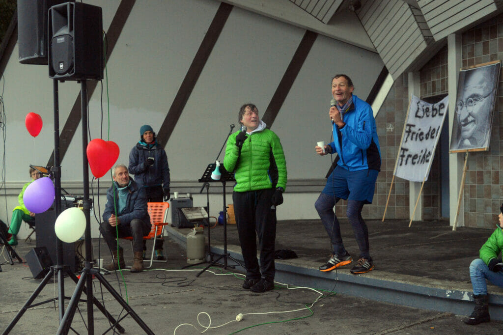 (v. li.) Friedensketteninitiator Gerry Mayr und sein Schweizer Ko-Organisator Jean Claude Greuter sind zur Demo durch den Regen gejoggt, um die Nachfolgeveranstaltung der Großversammlung anzukündigen. Nur dem Ordnungsamt möchten sie die Versammlung nicht melden. Das sei nicht notwendig, da es sich um den Zieleinlauf eines Halbmarathons handle, mit dem sie den Konstanzer Trichter füllen möchten.