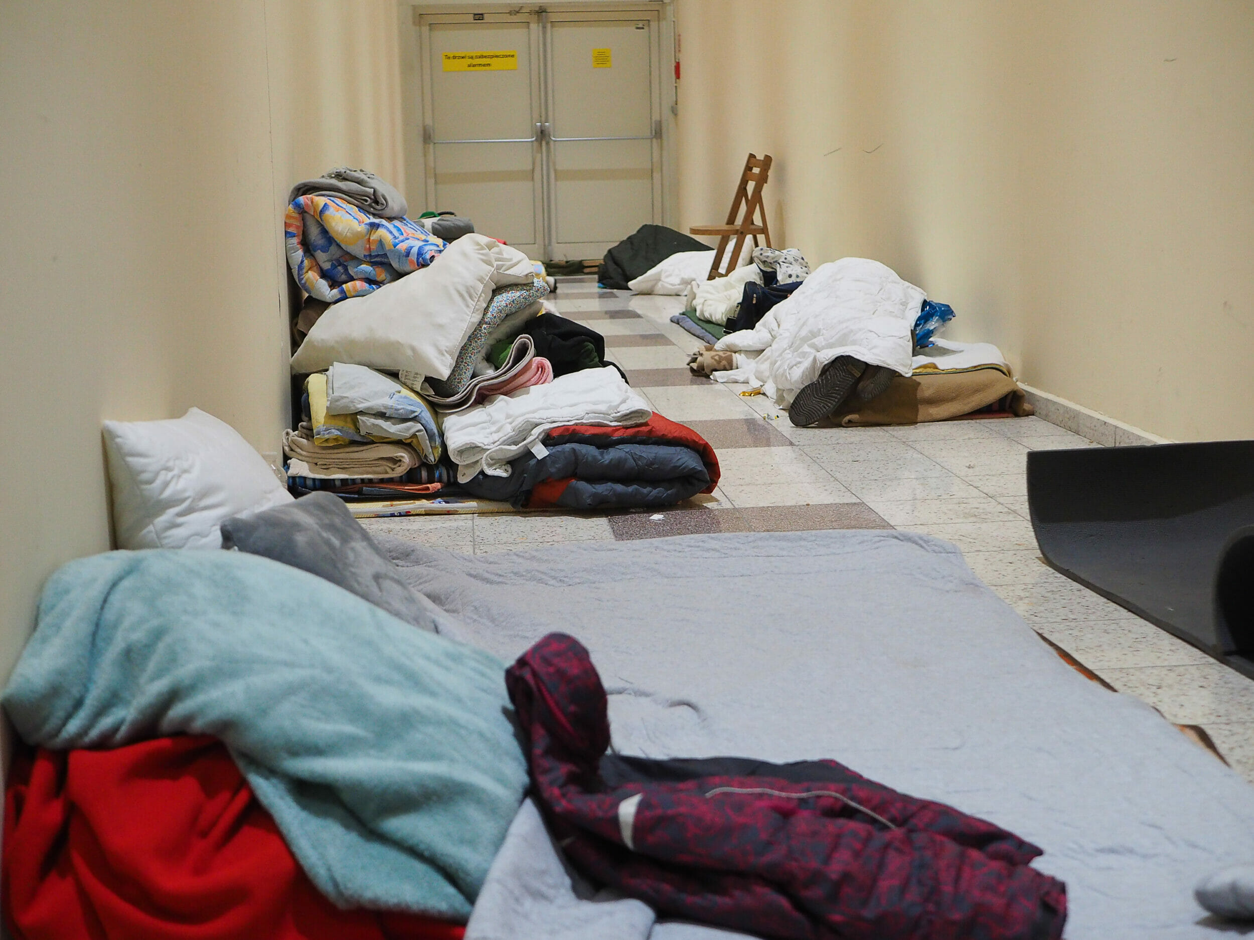 In einem Flur in einem leerstehenden Einkaufszentrum, in dem Menschen Essen und Infos erhalten ruht sich einer der Ankommenden aus. Als Notschlafplatz dienen hier Matten auf dem Boden.