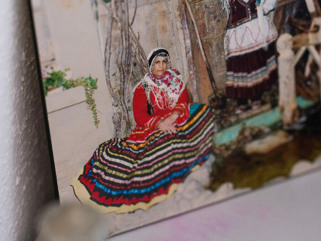 Ein Foto, das fast wie ein Gemälde wirkt: Es zeigt eine Frau in traditioneller Kleidung, die am Boden sitzt, ihr Oberteil ist Rot, der Rock ausgebreitet mit vielen Farbringen.